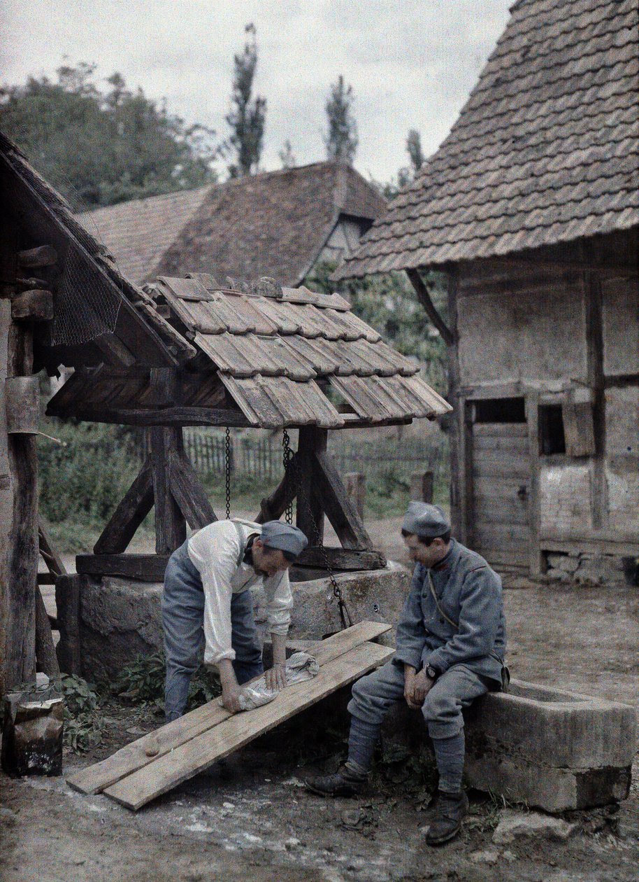 To franske soldater tager sig af deres vasketøj ved hjælp af brædder sat op på truget af et springvand nær en bondegård i byen Gildwiller, Department Haut-Rhin, Alsace, Frankrig, 21. juni 1917 (a af Paul Castelnau